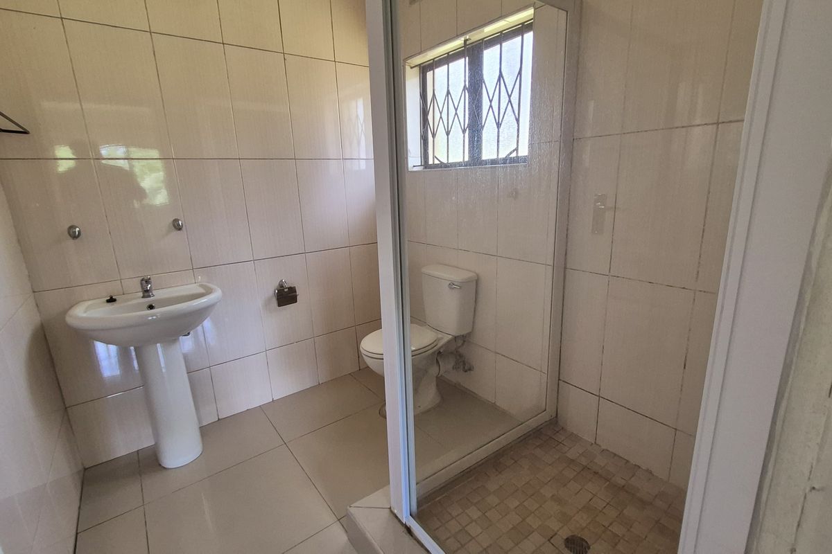 A functional bathroom featuring a pedestal basin, toilet, and a glass-enclosed shower with neutral wall and floor tiling.
