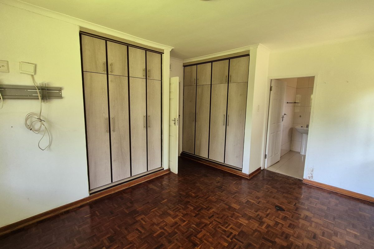 Spacious bedroom featuring classic parquet flooring and extensive built-in cupboard storage, with an adjoining en-suite bathroom access.