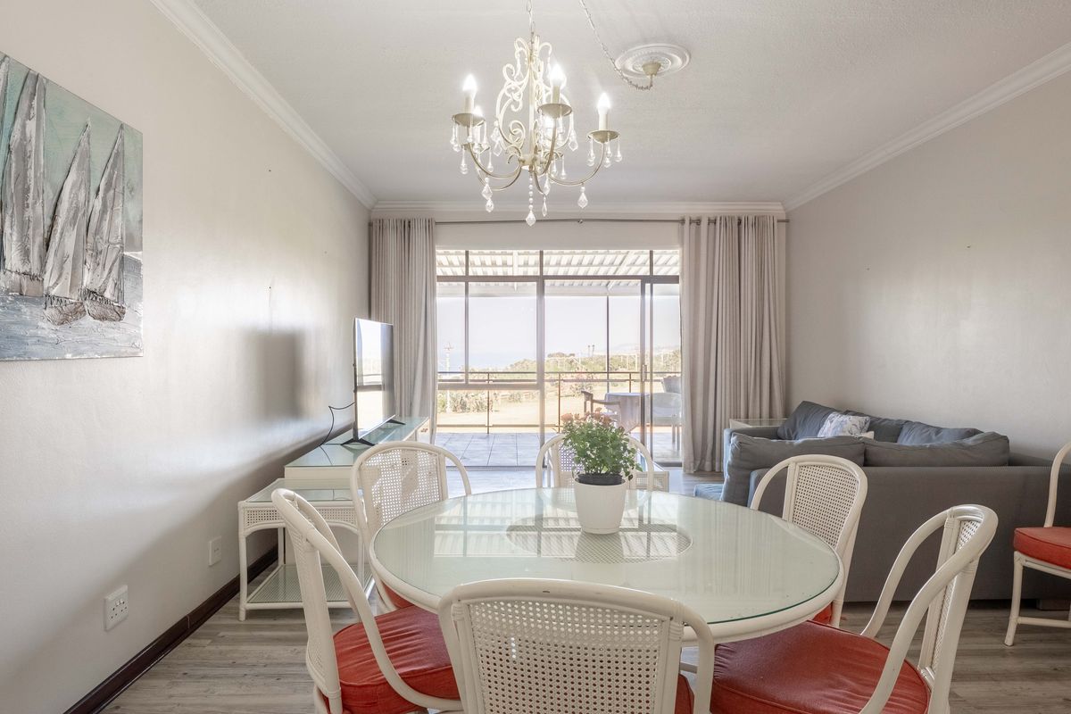 Bright living and dining area featuring laminate flooring, decorative ceiling rose, and large sliding glass doors leading to an outdoor balcony.