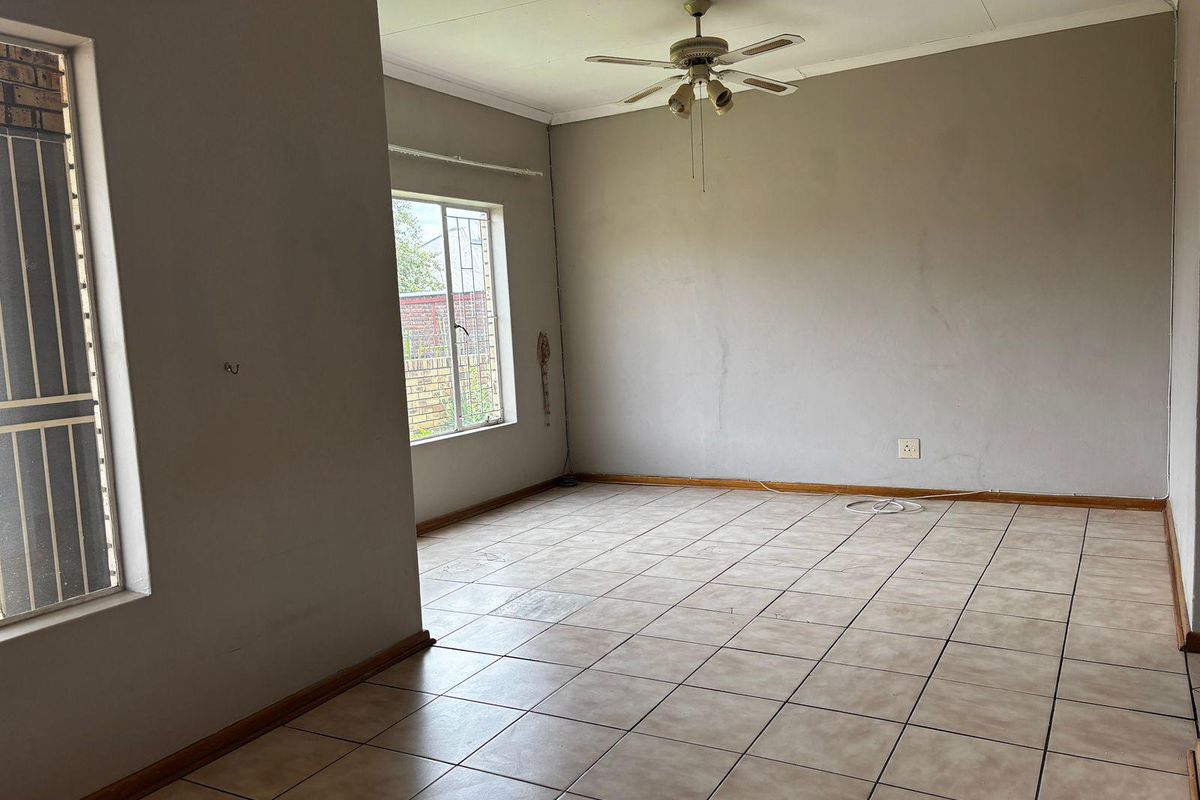 An empty living room featuring tiled flooring, a ceiling fan, and security bars on the windows.
