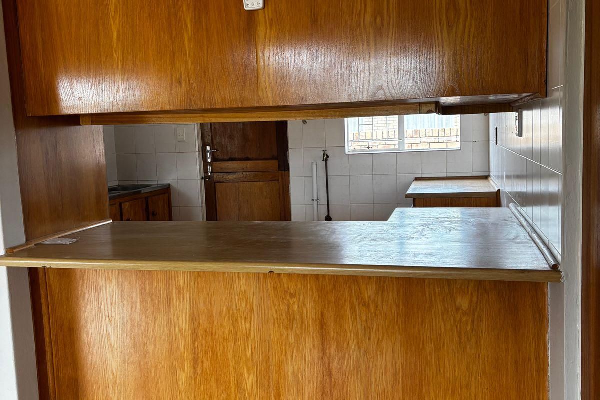 A dated kitchen featuring wood-veneer cabinetry, a breakfast bar counter, and tiled flooring, offering a functional layout ready for modernization.