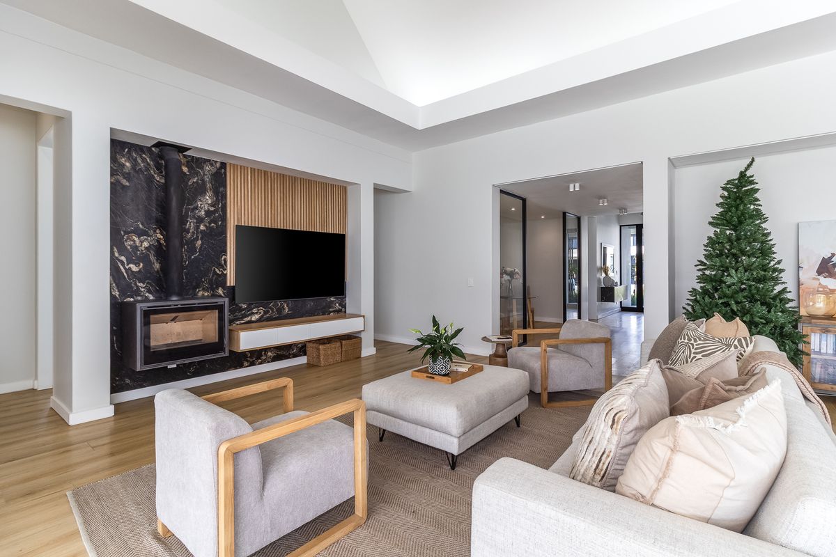 Modern living room featuring a striking marble-clad fireplace, timber slat feature wall, high vaulted ceilings, and light timber flooring.