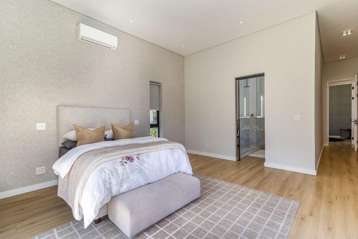 A modern, well-maintained bedroom featuring light wood-look flooring, a wall-mounted air conditioning unit, and an en-suite bathroom entrance.