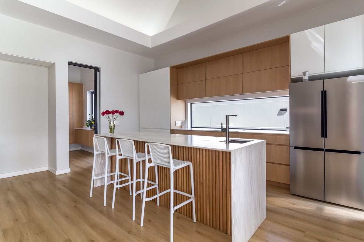 Modern kitchen featuring a marble-topped island with timber slat detailing, sleek cabinetry, integrated sink, and high-end finishes in a bright, open-plan space.