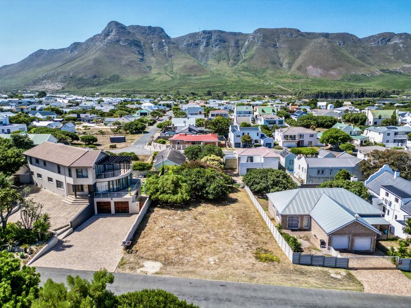 An aerial view of a vacant residential plot situated in a developed neighborhood with scenic mountain views in the background.