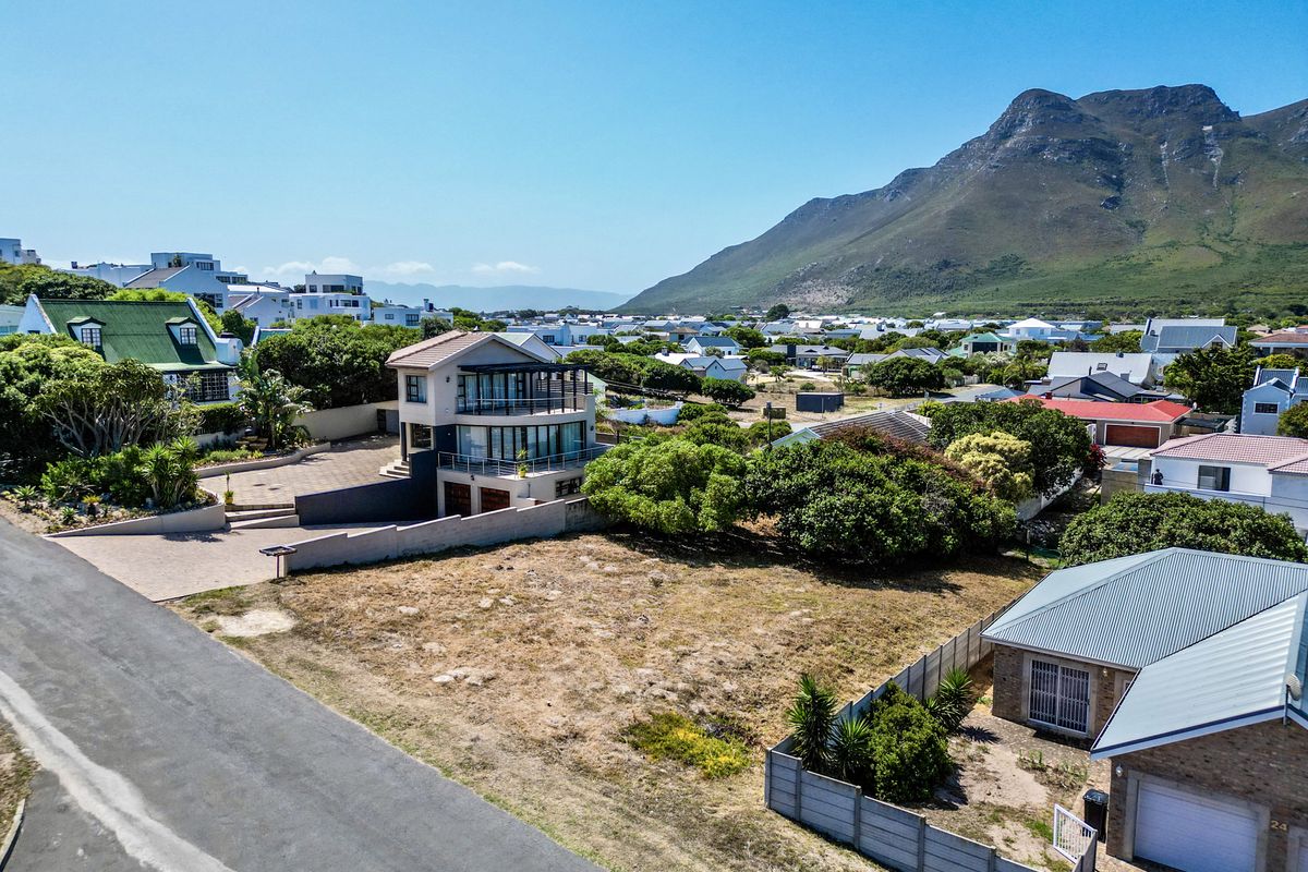 Aerial view of a vacant residential plot in a coastal neighborhood, featuring established boundary walls and proximity to local amenities and mountain views.