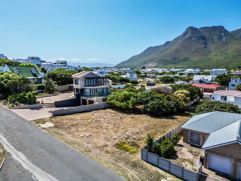 Aerial view of a vacant residential plot in a coastal neighborhood, featuring established boundary walls and proximity to local amenities and mountain views.