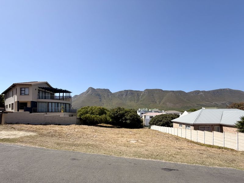 A vacant residential plot situated in a developed neighborhood, featuring clear mountain views and established boundary walls.