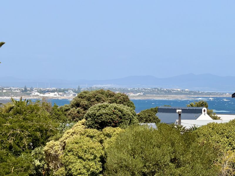 A scenic elevated view overlooking the coastline, ocean, and distant mountains, framed by lush greenery.