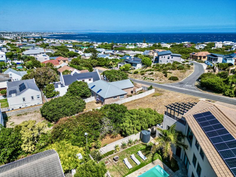 Aerial view of the residential property showing the surrounding neighborhood, coastal landscape, swimming pool, and existing infrastructure.
