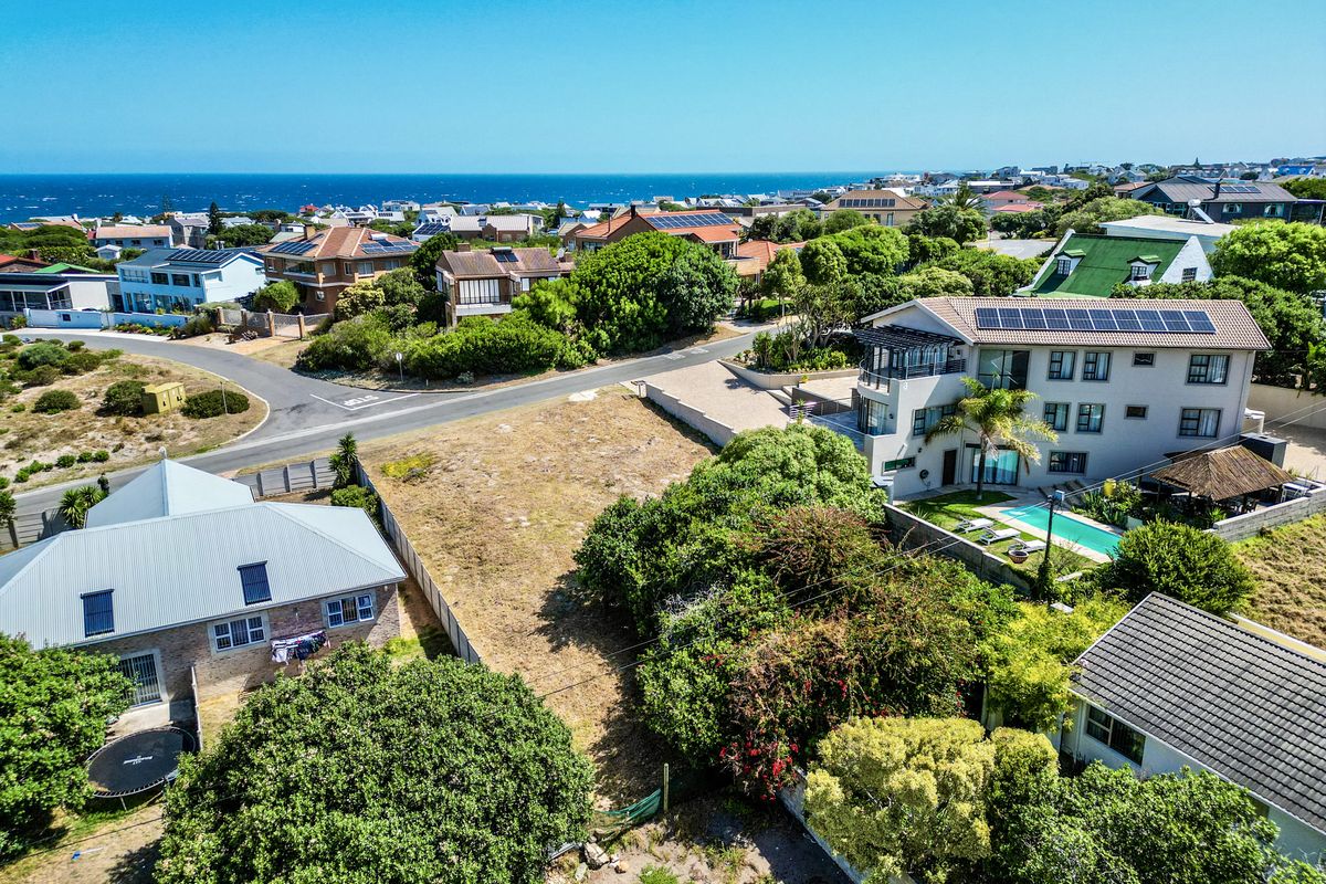 An aerial view of a vacant residential plot situated in a developed coastal neighborhood, surrounded by established homes and mature vegetation.