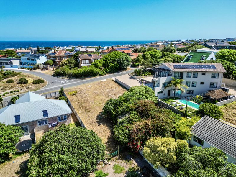 An aerial view of a vacant residential plot situated in a developed coastal neighborhood, surrounded by established homes and mature vegetation.