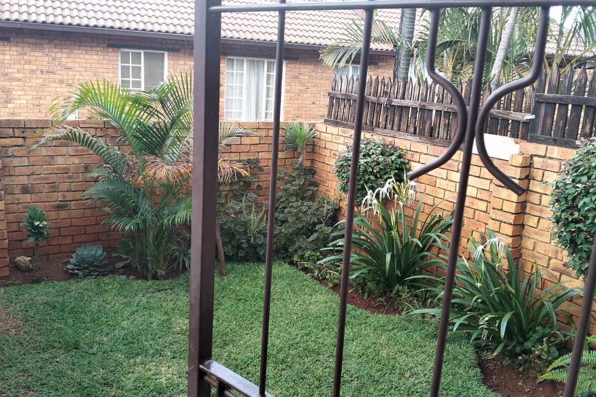 A private rear garden area featuring a small lawn, established garden beds, and perimeter brick walling with wooden fencing.