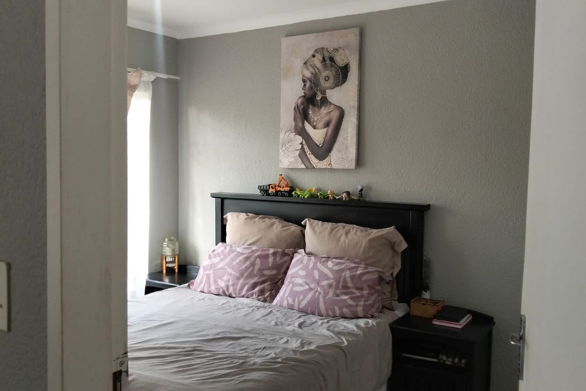 A bedroom featuring neutral grey walls and a window allowing natural light, viewed from the doorway.