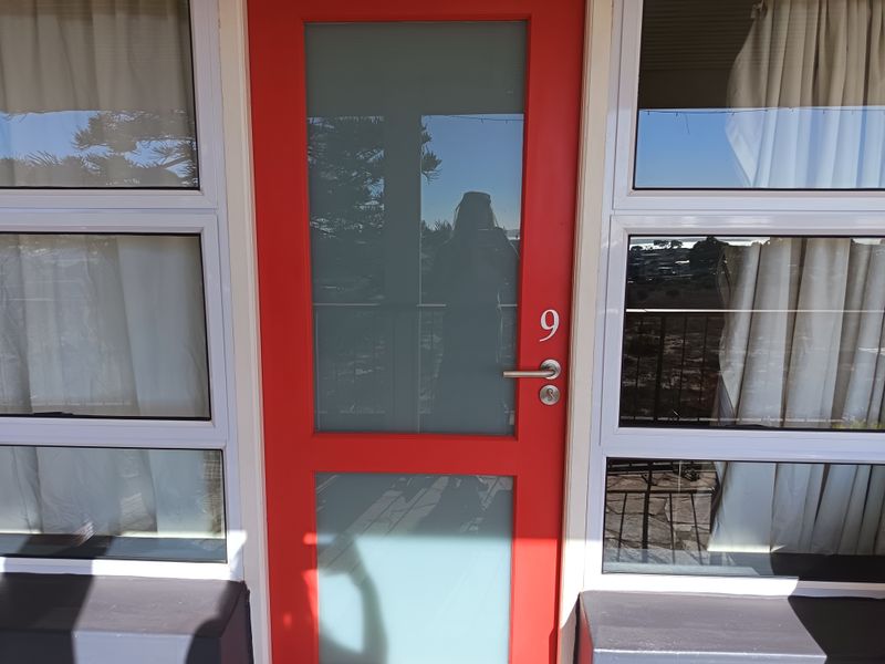 A bright red entrance door featuring frosted glass panels and modern lever hardware, flanked by large aluminium-framed windows.