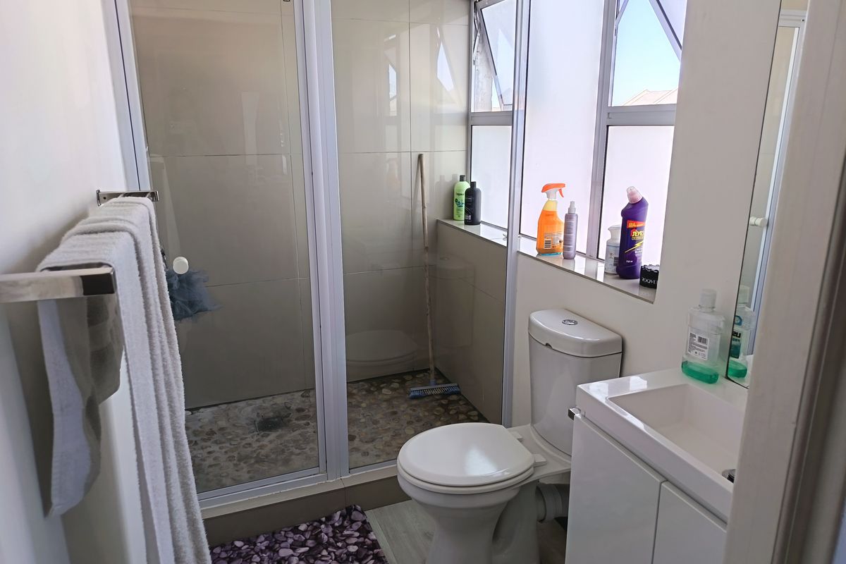 A functional bathroom featuring a shower enclosure with pebble flooring, a white toilet, and a vanity basin with storage.
