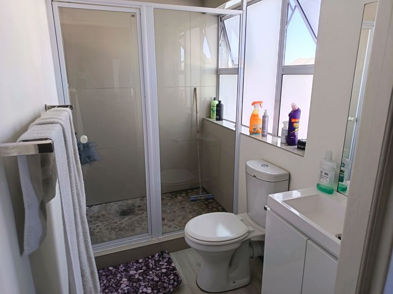 A functional bathroom featuring a shower enclosure with pebble flooring, a white toilet, and a vanity basin with storage.