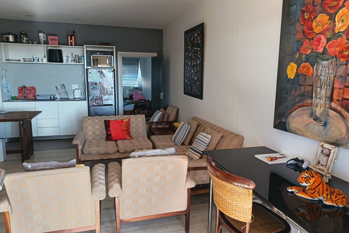 Open-plan living area featuring a compact kitchen with built-in cabinetry and laminate flooring, seamlessly connected to the main living space.
