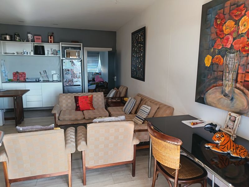 Open-plan living area featuring a compact kitchen with built-in cabinetry and laminate flooring, seamlessly connected to the main living space.