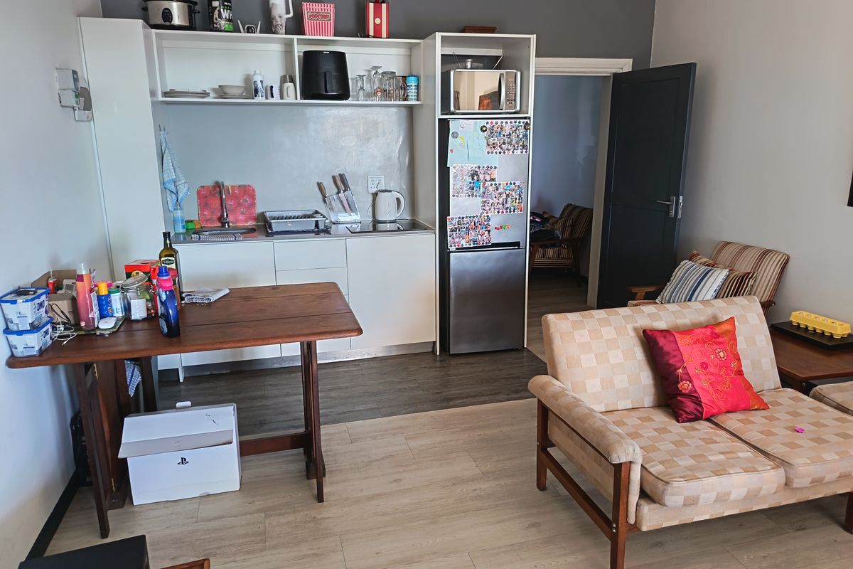 Open-plan living area featuring a compact kitchenette with built-in cabinetry, stainless steel sink, and light-toned laminate flooring throughout.