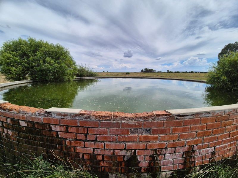 A circular brick-built farm reservoir or water storage tank set within an open landscape, showing signs of age and weathering.
