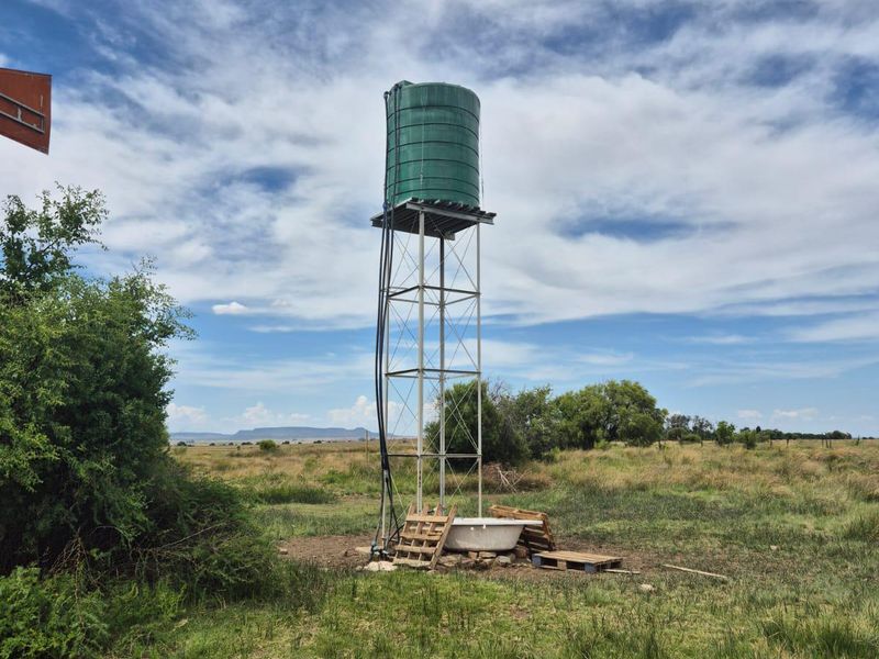 A raised green water storage tank mounted on a metal stand, situated in an open field on the farm property.