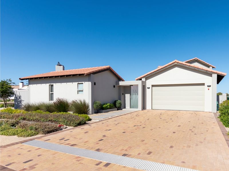 A well-maintained modern house featuring a paved driveway, double garage, and terracotta roof tiles, set within a neat landscaped garden.