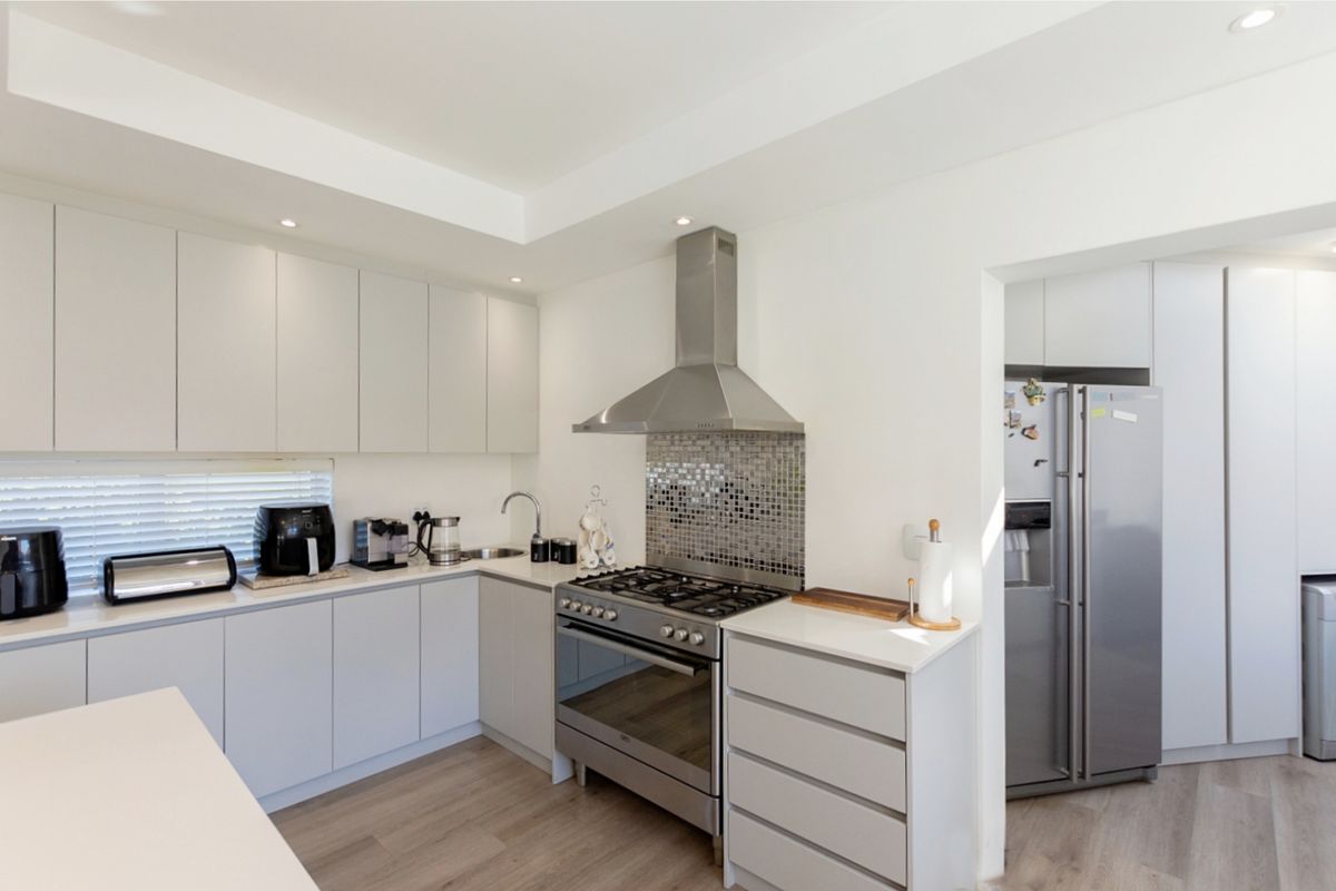 Modern kitchen featuring light grey cabinetry, stone countertops, a gas cooktop with stainless steel extractor, and a mosaic tile splashback.