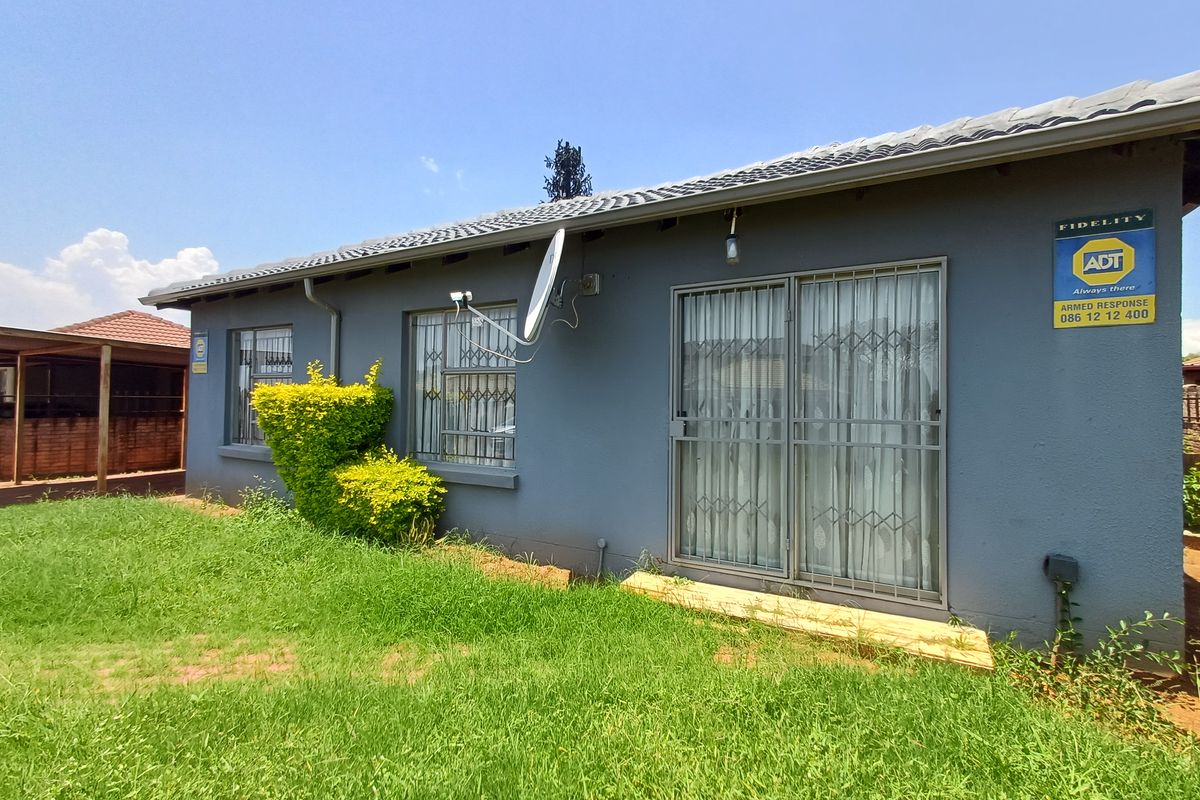 Rear exterior view of the house featuring a grey rendered facade, sliding glass doors with security gates, and a satellite dish.