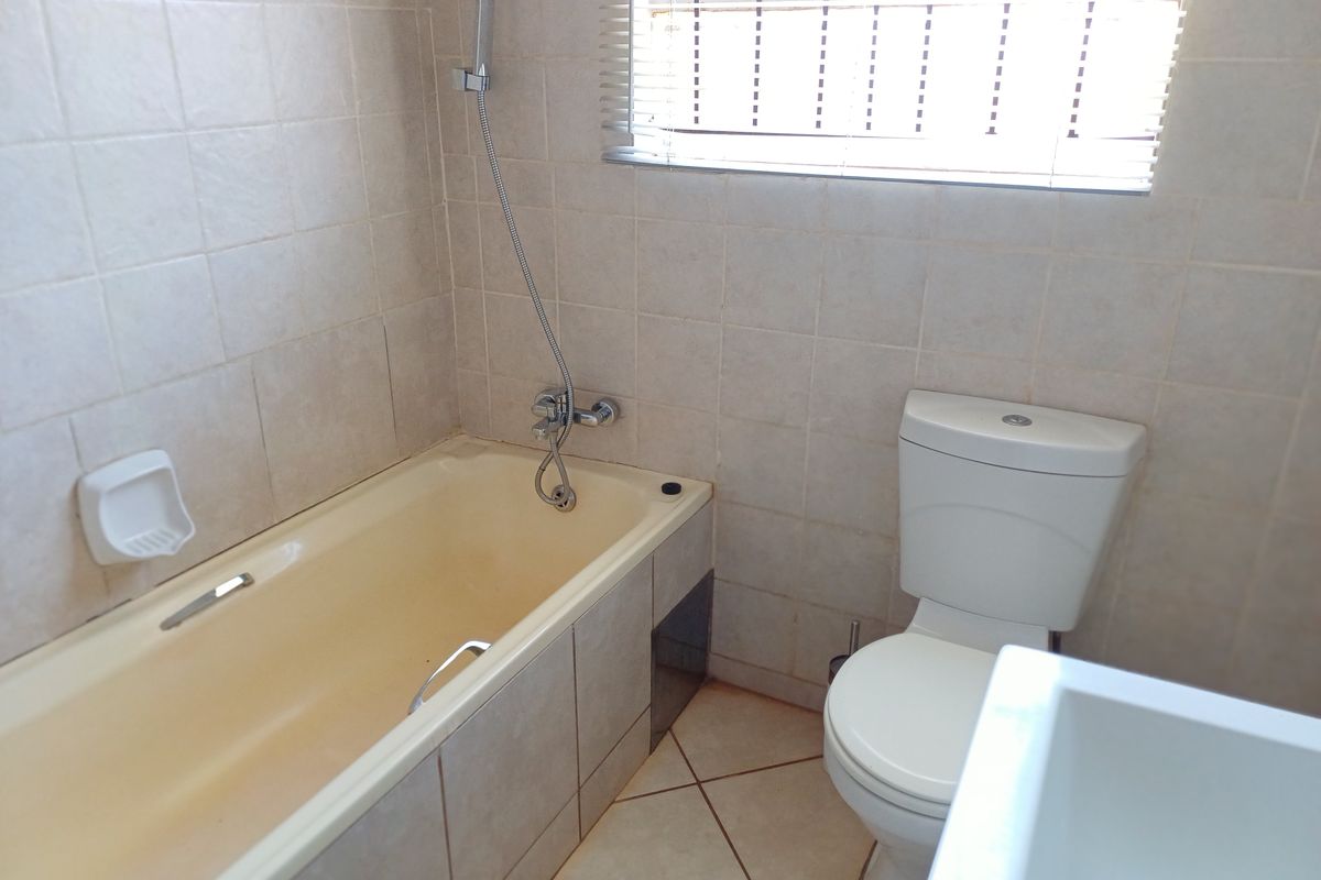 A functional bathroom featuring a bathtub with a handheld shower attachment, a standard toilet, and tiled walls and flooring.