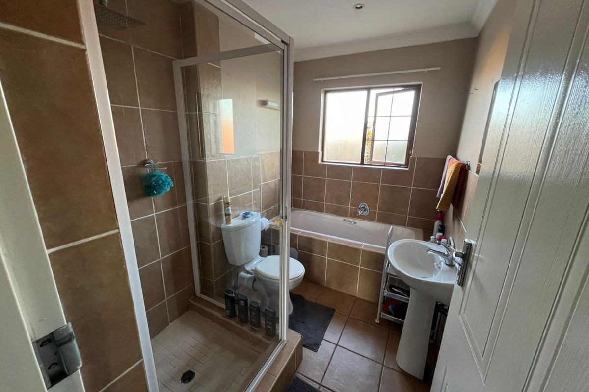 A functional bathroom featuring a glass-enclosed shower, a built-in bathtub, and a pedestal sink with neutral-toned wall and floor tiling.