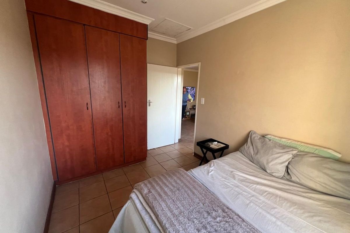 A bedroom featuring built-in wooden cupboards, tiled flooring, and crown molding, providing a functional living space.