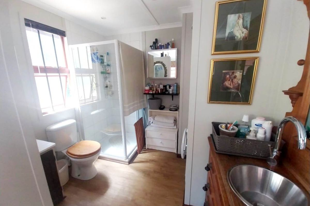 A functional bathroom featuring a shower enclosure, toilet, and a vanity basin with wood-look flooring.