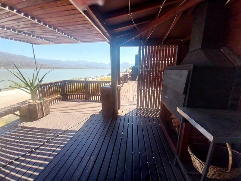 Spacious timber deck featuring a built-in braai, pergola covering, and scenic waterfront views.