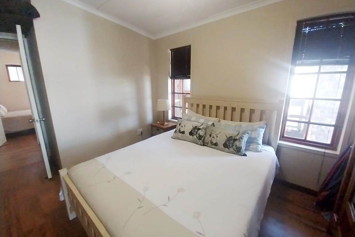A cozy bedroom featuring timber flooring, natural light through timber-framed windows, and classic cornicing details.