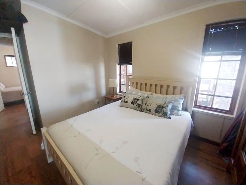 A cozy bedroom featuring timber flooring, natural light through timber-framed windows, and classic cornicing details.