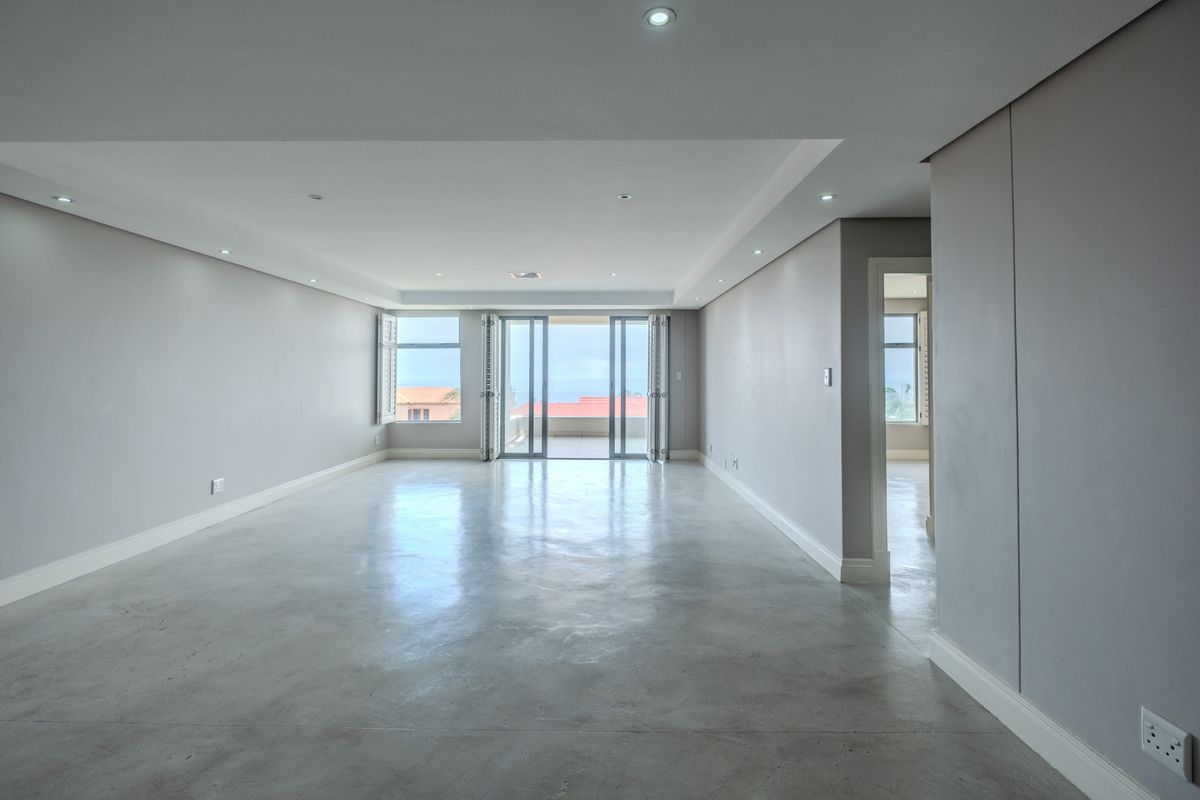 Spacious, open-plan living area featuring polished concrete floors, recessed lighting, and bi-fold doors leading to an outdoor balcony with coastal views.