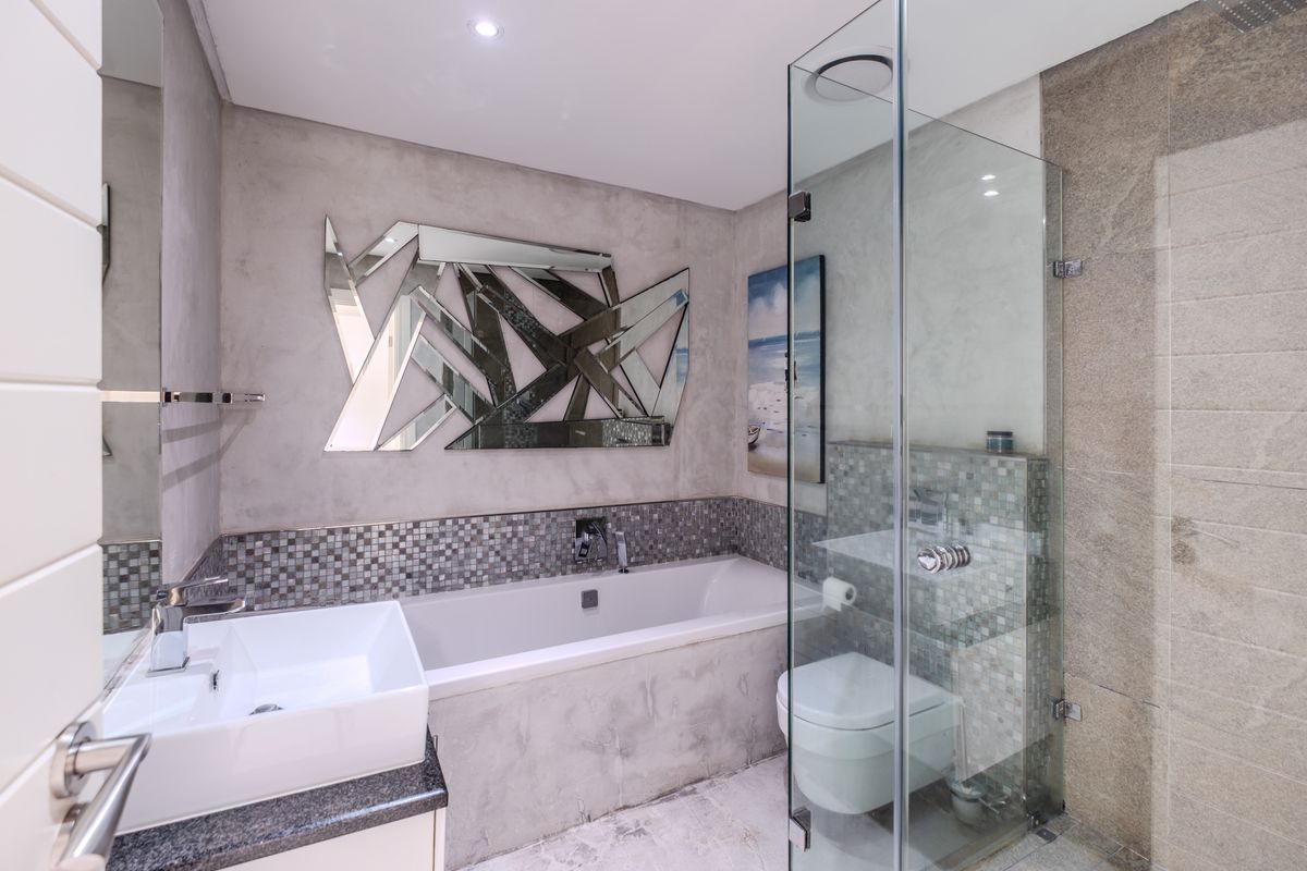 Modern bathroom featuring a built-in bathtub, glass-enclosed shower, wall-mounted toilet, and contemporary stone-look wall finishes with mosaic tile accents.