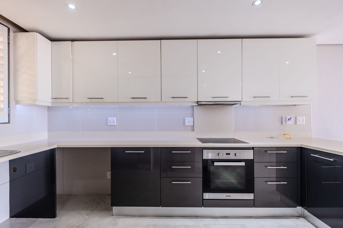 Modern kitchen featuring high-gloss cabinetry, integrated oven and hob, stone countertops, and a clean tiled backsplash in a bright, contemporary space.