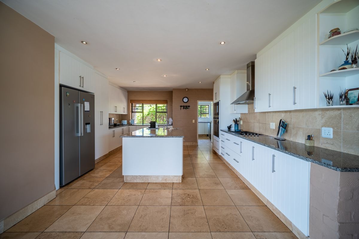 Spacious kitchen featuring a central island, granite countertops, built-in cabinetry, gas hob, and stainless steel extractor fan with tiled flooring throughout.