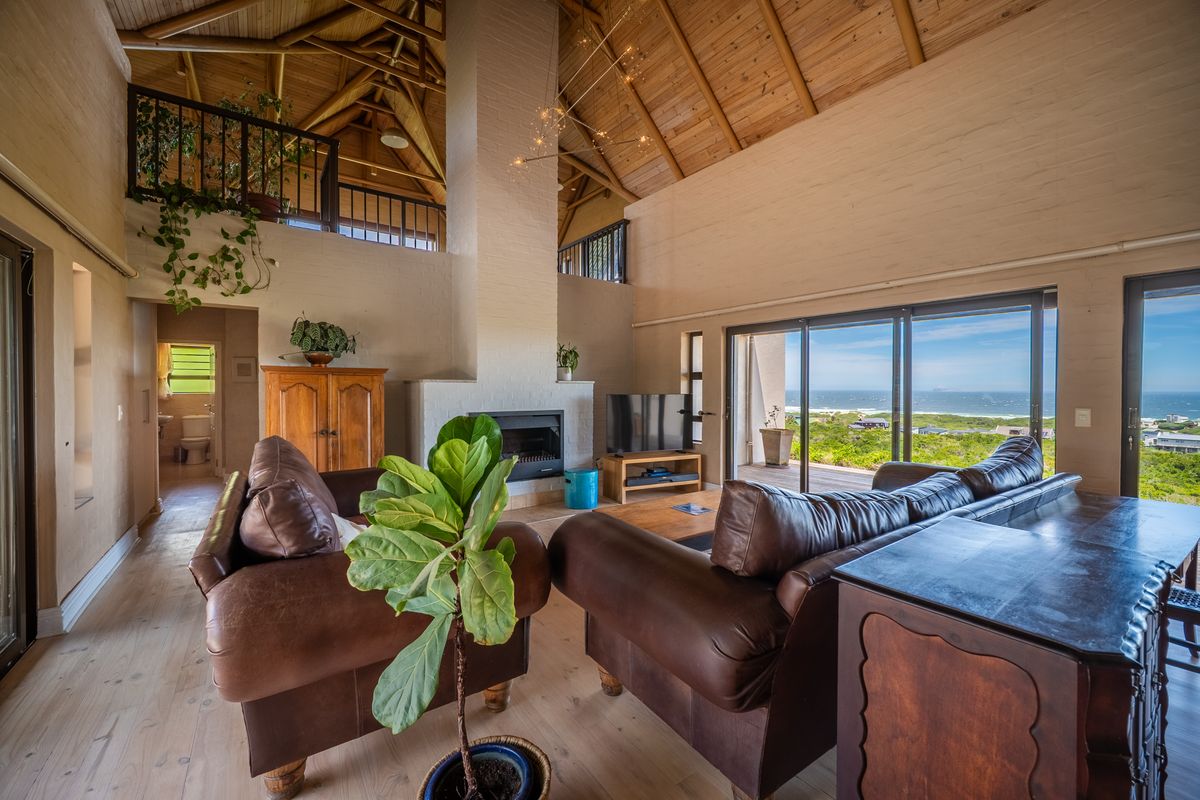 Spacious living room featuring a high vaulted timber ceiling, exposed trusses, a built-in fireplace, and large sliding doors opening to a scenic coastal view.