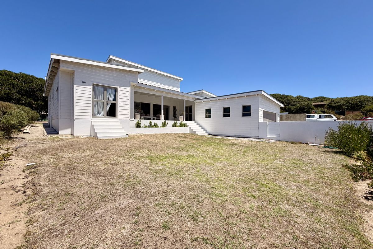 Rear view of a modern white weatherboard house featuring a covered patio, concrete steps, and a spacious backyard area.