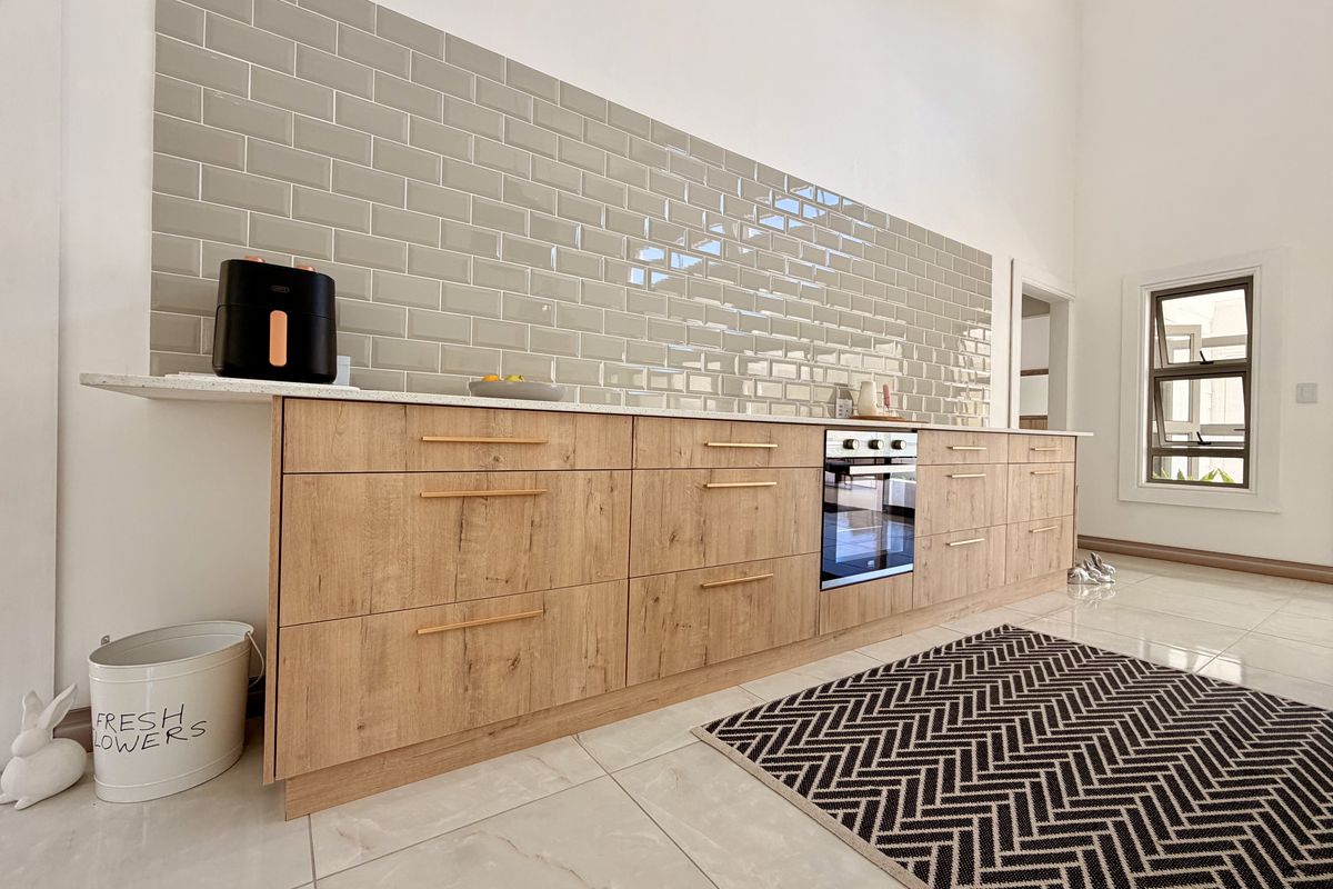 Modern kitchen featuring light wood-look cabinetry, stone countertops, and a stylish grey subway tile backsplash with integrated oven.