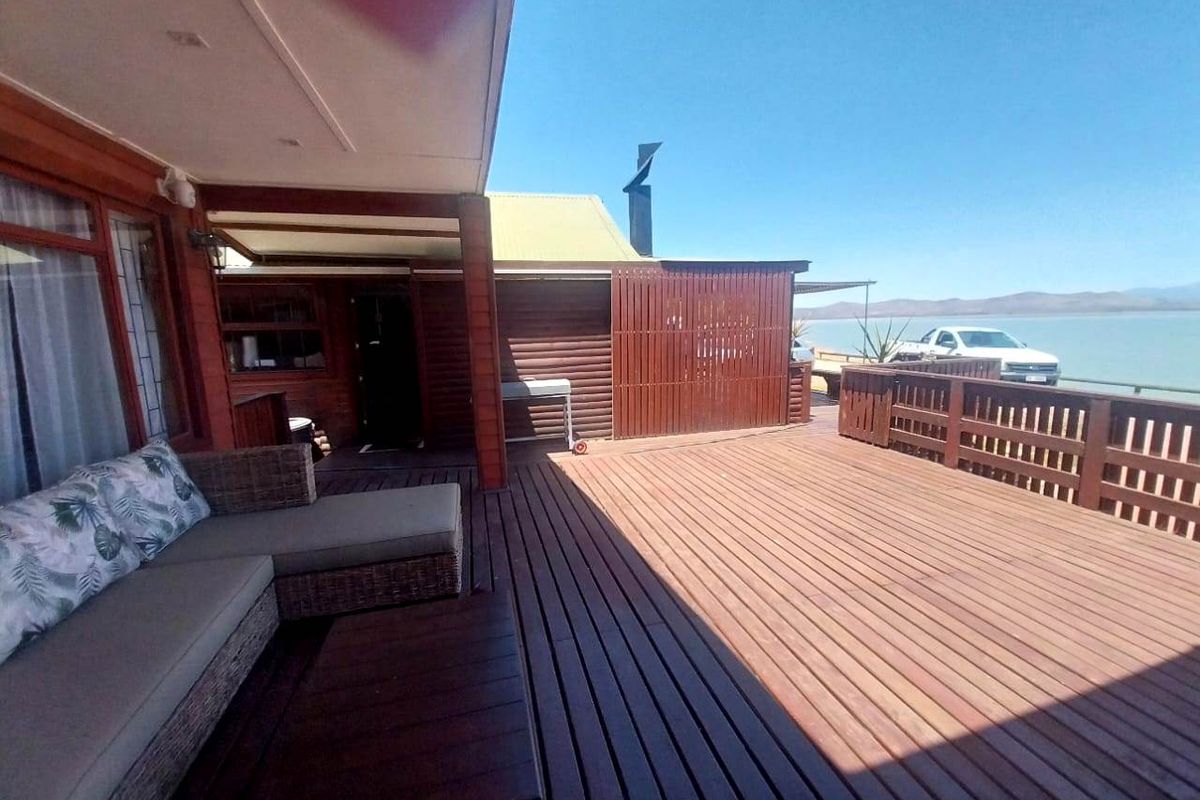 Spacious wooden deck patio featuring a covered area and open space, offering scenic water views and integrated timber railings.