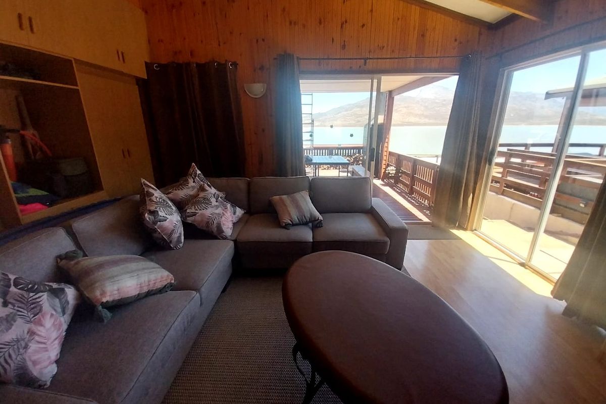 Spacious living room featuring timber-clad walls, vaulted ceilings, and large sliding glass doors opening onto a scenic deck with water views.