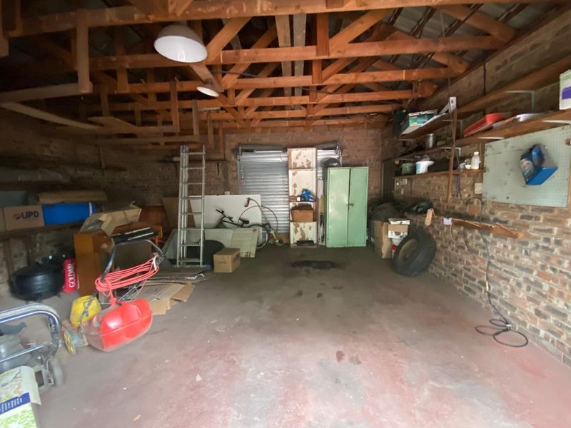 A spacious garage featuring exposed timber roof trusses, brick walls, and a concrete floor, offering ample storage potential.