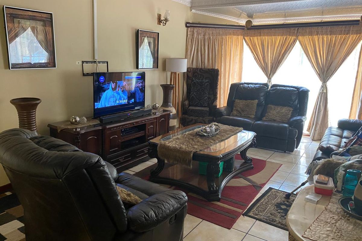 A spacious living room featuring tiled flooring, decorative ceiling cornices, and large sliding glass doors that provide ample natural light.