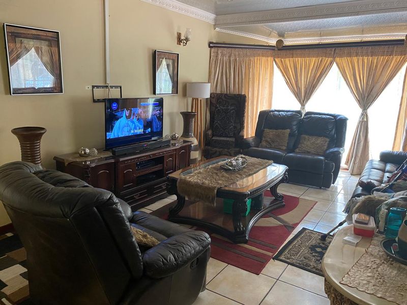 A spacious living room featuring tiled flooring, decorative ceiling cornices, and large sliding glass doors that provide ample natural light.