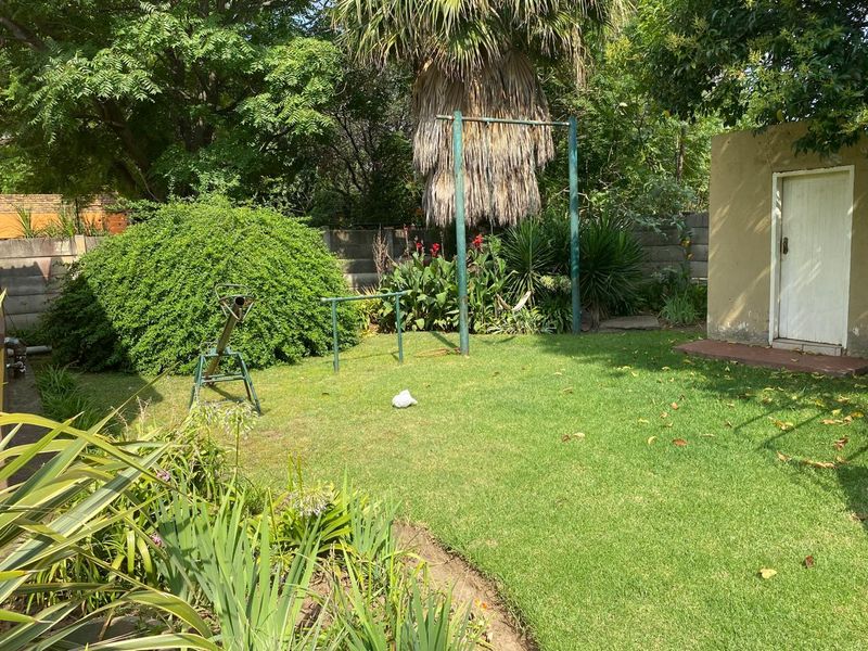 A private garden area featuring a well-maintained lawn, mature landscaping, and a small outbuilding with a secure door.