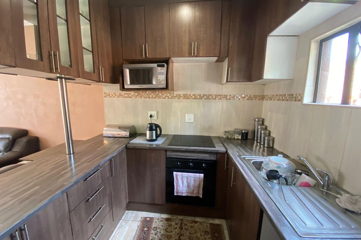 Compact kitchen featuring dark wood-finish cabinetry, laminate countertops, a built-in oven with electric hob, and a stainless steel sink.